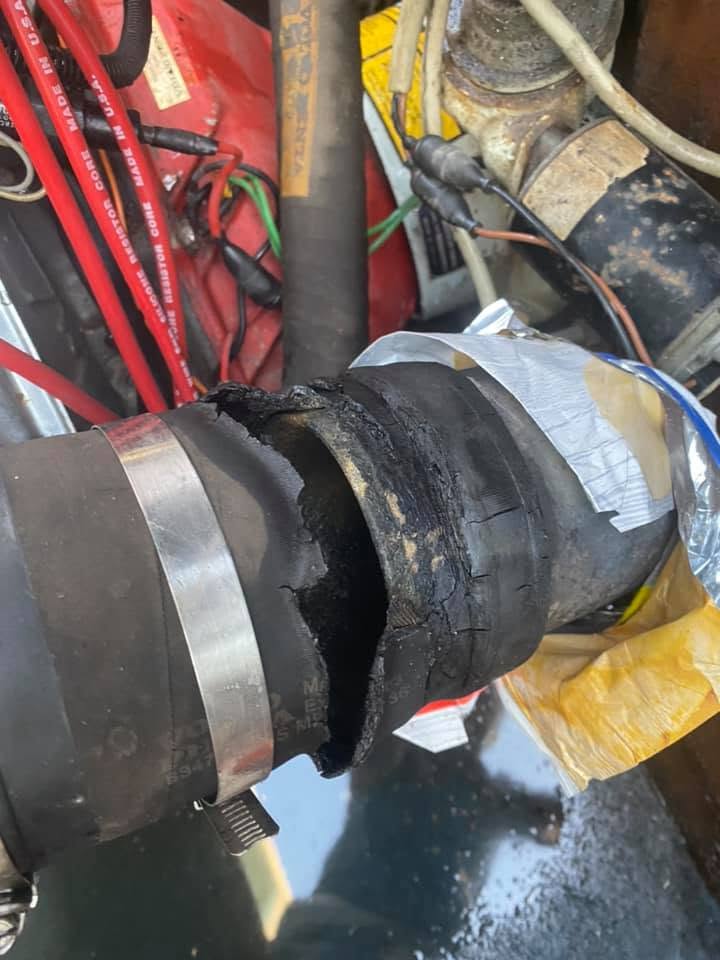 A section of marine exhaust hose burned through to crumbling charcoal between two hose clamps, foil and a chip bag already wrapped around the section beyond it