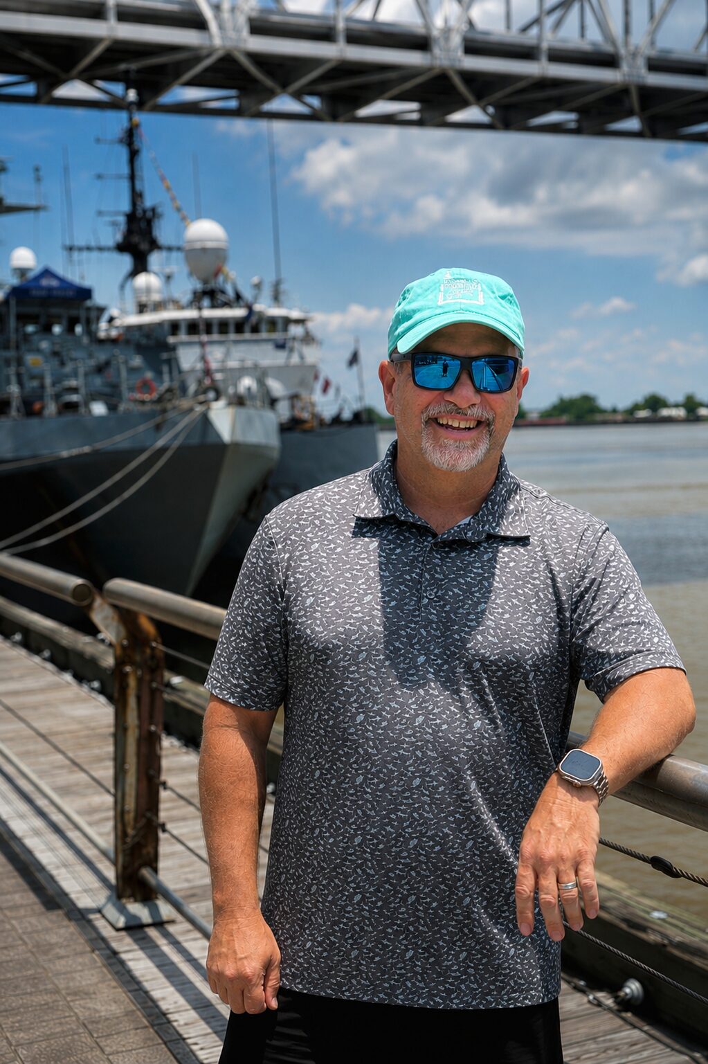 Nate Eckler at a dockside rail with a moored naval vessel behind him
