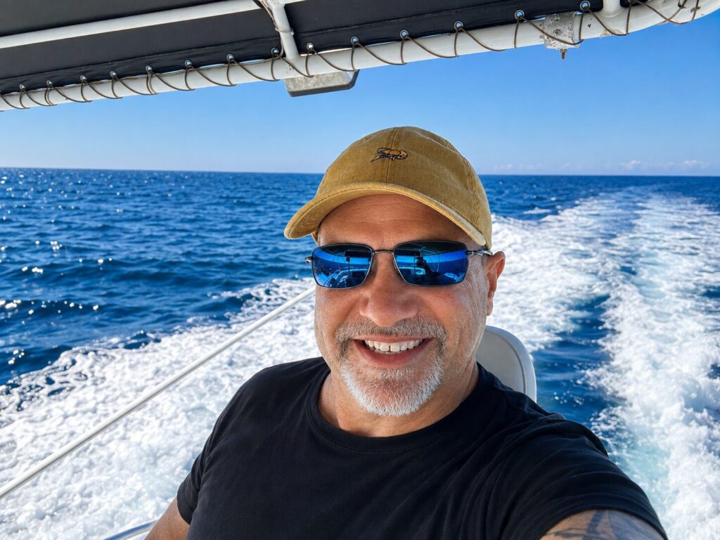 Nate Eckler under way offshore in a ball cap and sunglasses, the vessel's wake and open blue water behind him