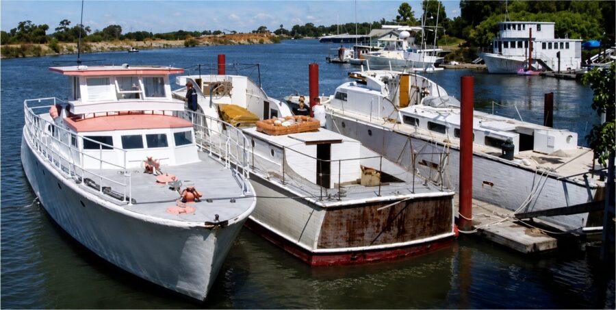 Neptune, Avenger and Phoenix moored side by side at a river dock: three wooden World War II-era crash rescue boats, the middle one with a rust-streaked transom
