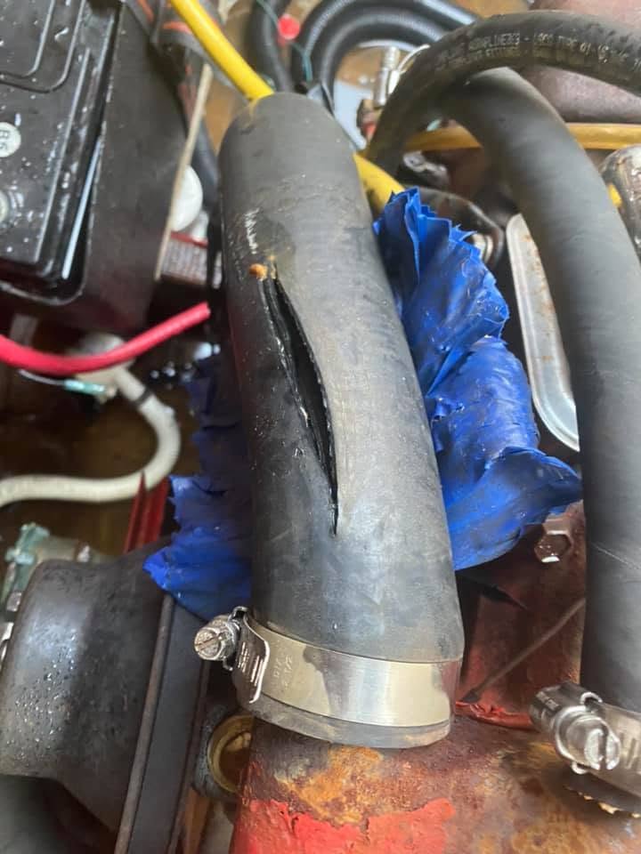 A black rubber hose with a long split running down its length, clamped to a fitting on a red engine block